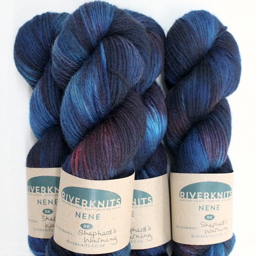 A pile of skeins of Nene DK in variegated deep blues, teals, and burgundy red