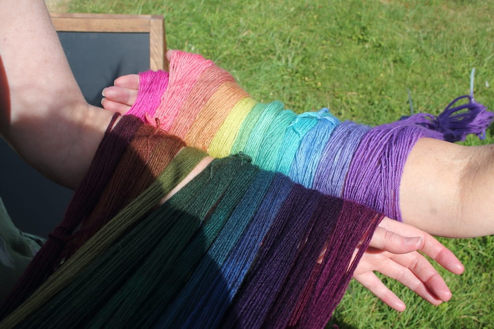 Two arms with hand dyeing rainbows of yarn hanging on them